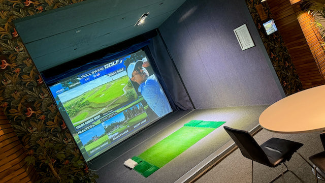 Snett fotograferad bild av en golfsimulator med en projicerad på skärmen och en grön liten slagbana i förgrunden