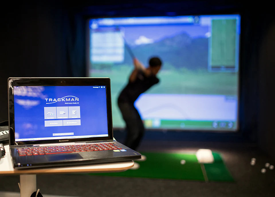 Närbild på Trackman-display och i bakgrunden svingar en person golfklubban mot en stor simulator skärm.
